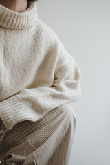 Closeup view of pretty young woman wearing warm knitted sweater pullover over white wall. Aesthetic fashion vogue composition. Neutral pastel beige color