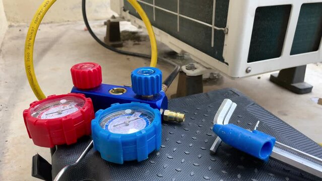 Air conditioner repair works on home unit. Blue collar worker. Technician is checking air conditioner ,measuring equipment for filling air conditioners.