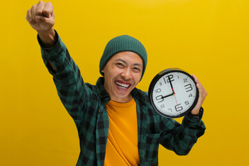 Young Asian man, dressed in a beanie hat and casual shirt, celebrates success with a raised arm in...