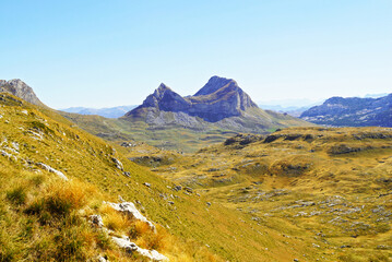 View of the peak of Sedlenha Greda in Durmitor National Park in Montenegro. Autumn landscape with a mountain with two picturesque peaks separated by a pass, and a mountain valley with yellowed grass