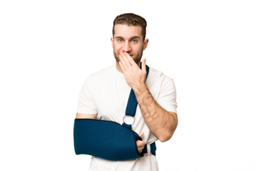 Young handsome blonde man with broken arm and wearing a sling over isolated chroma key background happy and smiling covering mouth with hand