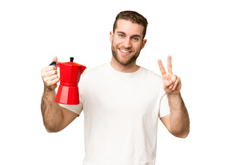 Young handsome blonde man holding coffee pot over isolated chroma key background smiling and...