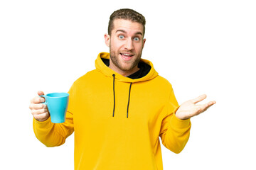 Young handsome blonde man holding cup of coffee over isolated background with shocked facial...