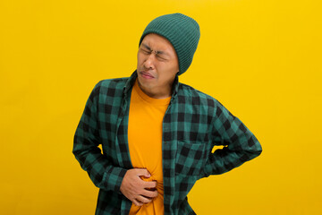 Unhappy Asian man is holding his belly in pain, visibly suffering from a stomachache, likely due to...