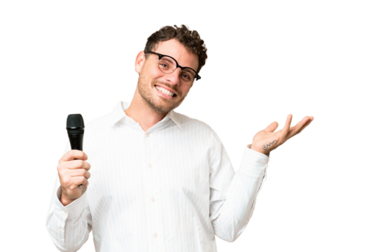 Brazilian man picking up a microphone over isolated chroma key background extending hands to the side for inviting to come - Powered by Adobe