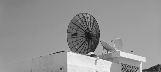 Monochrome Image Of Satellite Dishes On White Rooftop Against Clear Sky
