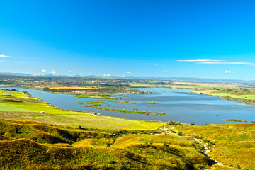 Panoramic view of cliffs and meadows on a sunny spring day with a lake in background.