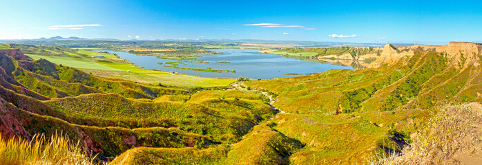 Panoramic view of cliffs and meadows on a sunny spring day with a lake in background.