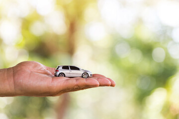Man hand holding a car model on bokeh sunlight in the public park, Loan for buy a new car or business investment a chattel in the future concept.