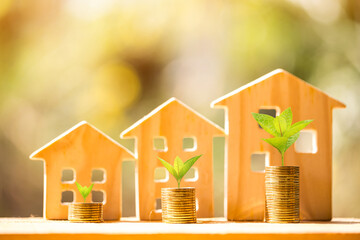 Stack coin with plant growing and the wooden home model for family put on the wood in the public park, Business investment loan for real estate or save money for buy new house in the future concept.