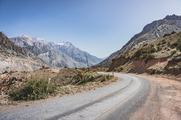 The road winds in a mountain valley in the Fan Mountains in Tajikistan, a mountain road in the highlands among rocks and cliffs