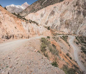 A dusty road winds in a mountain valley in the Fan Mountains in Tajikistan, a mountain road in the highlands
