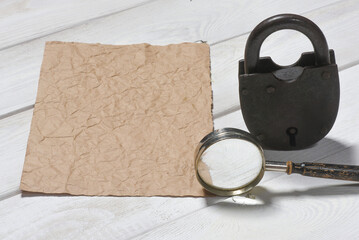 Old padlock, magnifying glass and blank paper sheet page with copy space on the wooden desk table...