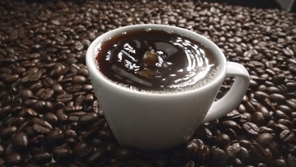 Close up of coffee bean drop in to hot espresso with pile of coffee seed. Macro of freshly roasted...