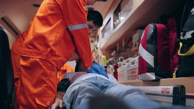 Asian man emergency medical technician (EMT) or paramedic nurse is performing CPR on a patient in an ambulance car