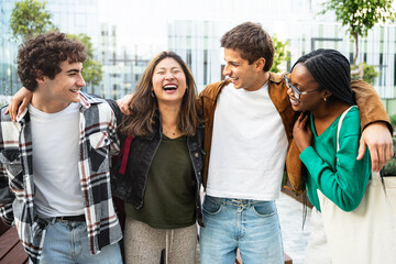 Four young friends hugging each other outdoors - Happy multiracial students laughing in the city 
