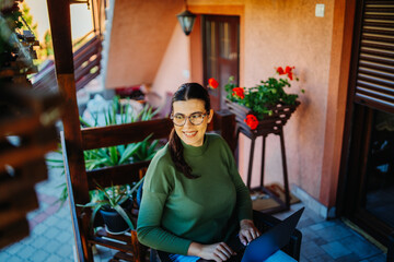 One young caucasian woman is working on her laptop from home on her balcony 