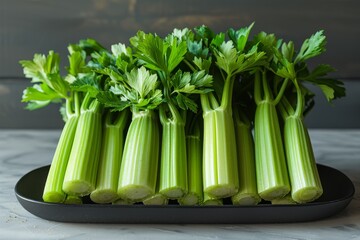 A bunch of bright green celery stalks neatly lined up on a dark tray, with a textured background