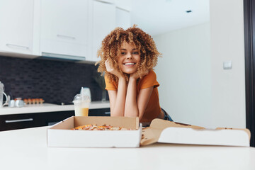 Young woman with curly hair eating pizza on kitchen counter, lifestyle concept
