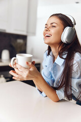Young woman with headphones enjoying music and coffee in the cozy kitchen at home