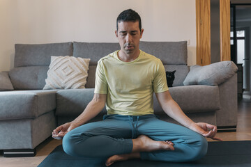 Man Practicing Mindfulness on Yoga Mat in Living Room. Man in dignified posture meditates with...