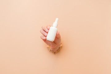 White bottle with serum lotion or essential oil (hyaluronic acid and collagen) in hand on beige...