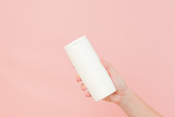 Shampoo, hair conditioner or body lotion bottle in hands in pink background. Cosmetics bottle
