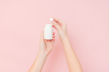 Obraz na płótnie Canvas White bottle plastic tube in woman's hands on pink background. Packaging for pills, capsules or supplements. Cosmetics