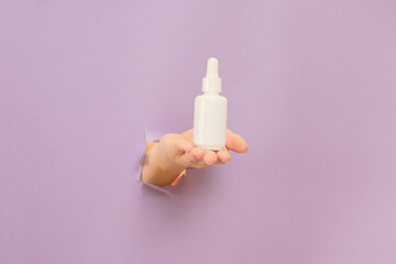 Hand holding glass bottle with dropper lid. White container with cosmetic product, serum (essential...