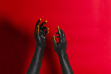 Black and gold colors painted woman's hands on her skin with red background. High Fashion art concept