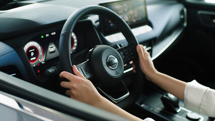 Happy adult female buyer - businesswoman - enjoying buying a new, modern electric car at a car dealership. The concept of an expensive purchase, rental and test drive.