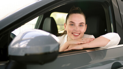 Happy adult female buyer - businesswoman - enjoying buying a new, modern electric car at a car dealership. The concept of an expensive purchase, rental and test drive.