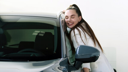 Happy adult female buyer - businesswoman - enjoying buying a new, modern electric car at a car dealership. The concept of an expensive purchase, rental and test drive.