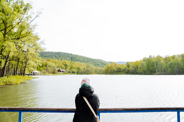 A woman admiring the lake from a bridge among the natural landscape