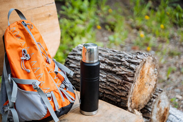 A bag and a bottle rest on a wooden bench in a grassy landscape