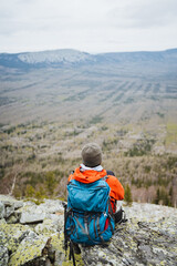 Hiker with backpack rests on rock, gazing at valley below in serene landscape