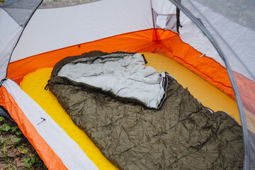 A sleeping bag rests inside a tent on the grassy slope under the shade of a roof