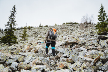 Hiker climbs rocky hillside with backpack under blue sky
