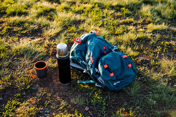 Backpack, thermos, and cup resting in the grassy landscape