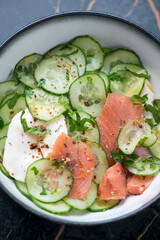Bowl of cucumber salad with smoked salmon and poached egg, vertical shot, close-up, selective focus