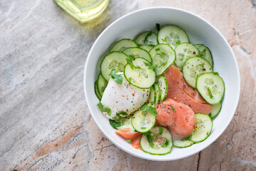 Bowl with smoked salmon and cucumber salad, horizontal shot on a grey and roseate granite background with space, high angle view