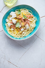 Turquoise bowl with smoked salmon and feta spaghetti, vertical shot on a white granite background, high angle view, copy space