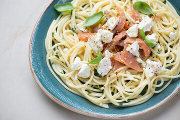 Lemony spaghetti with smoked salmon, feta cheese and fresh basil on a blue plate, horizontal shot, middle close-up