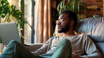Fototapeta premium A young man is sitting on the couch and looking at his laptop