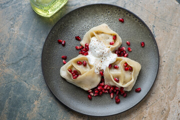 Steamed manti served with pomegranate seeds and yogurt, horizontal shot on a beige and grey granite...
