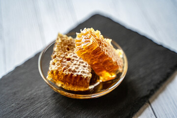 natural honey in a honeycomb, a juicy appetizing piece lies on a transparent plate on crumpled craft paper on a wooden background