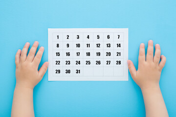 Baby boy hands and white calendar on light blue table background. Pastel color. Closeup. Waiting...