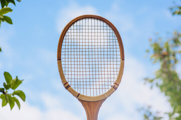 Closeup photo of a sports wooden retro tennis racket against the sky outdoors.