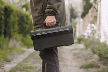A man, a professional worker, a repairman holds a suitcase in his hands, a briefcase with tools,...