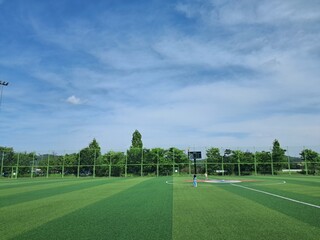 soccer field and goal, Photo of sports park, artificial turf soccer field, safety fence, trees and blue sky with clouds